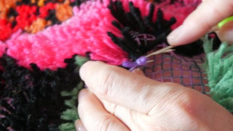 Hand embroidered carpet. A woman using a special hook and thread embroiders a carpet with purple threads. Handmade carpet embroidery. Women's hands create a pattern using multi-colored threads.
