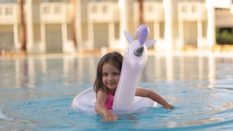 Child in swimming pool on unicorn inflatable violet ring. Little girl learning to swim with float. Water toy for baby and toddler. Healthy outdoor sport activity for children. Kids beach fun.