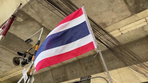 Thai flag flapping in breeze waving in the wind with high electrical wire and railway barrier background. Thai national patriotism concept. Low angle shot daytime. Travel concept