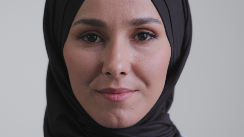 Close-up arabian human female face islam woman with natural makeup clear skin attractive pretty muslim girl wearing traditional hijab scarf standing indoors front looking at camera confident eyesight | Shutterstock HD Video #1089624933