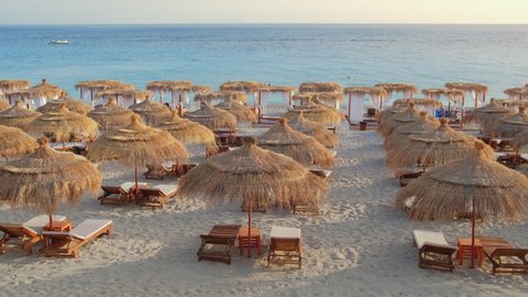 Beautiful beach with umbrellas and sunbeds. Perfect summer vacation destination. Straw sunshades and sunbeds on the empty beach with sea in the background.