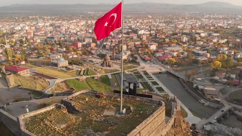 Aerial view of the Turkish flag over the castle of Kars in Turkey. Cityscape of the Kars city at background. Flag of Turkey waving in the wind. Flying around Turkish flag close-up.