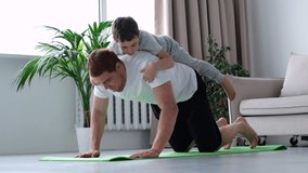 happy father doing push up exercise with son on back at gym. little boy hugs dad from behind. 4k video footage slow motion.