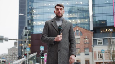 TV News Live Reportage: Presenter Holding Microphone Talking while City in Background. Economy, Business, City, Journalistic Investigation. Television Program Channel Playback. Static Medium Shot