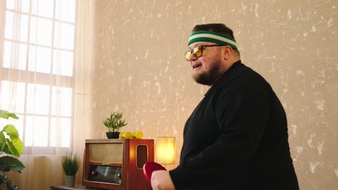 Charismatic fat man doing sport at home he playing the ping pong at home very excited he catch the ball with the racket and get excited he wearing the sun glasses. Shot on ARRI Alexa Mini