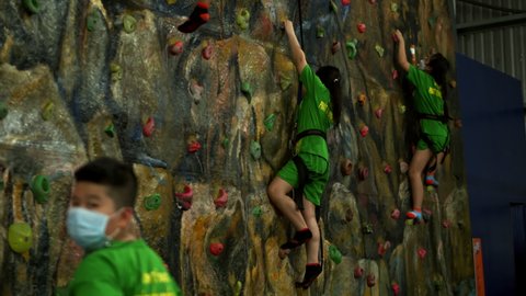 Children is training on the climbing wall with an instructor. Children's rock climbing in private school.Climbing exercises.School-age children climbs wall climbing wall.Saigon, Vietnam, April 6, 2022