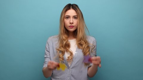 Positive attractive woman holding two pieces of puzzle, colorful jigsaw, metaphor of unity connection, complete solution, wearing striped shirt. Indoor studio shot isolated on blue background.