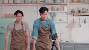 Asian gay couple using mobile phones create new content with live broadcasting cooking through social media in home kitchen. influencer streaming lifestyle and daily routine for fan club.