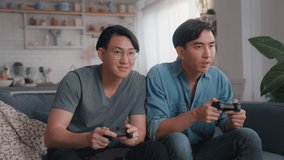 Slow motion of Two young Asian homosexuals Sitting on the Sofa Playing use a joystick to play Online Video Games Together at Home. Happy young people playing video games on console
