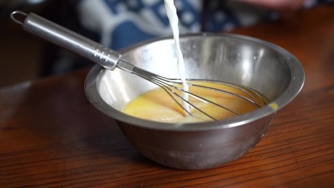 A woman pouring milk into egg juice
