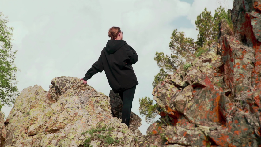 A rear view of a girl sitting on rocks in the mountains and looking into the distance. Tourism