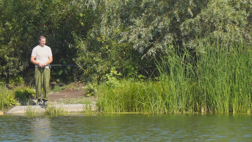 A fisherman on the shore of a lake or river with a fishing rod catches fish. Camera panning