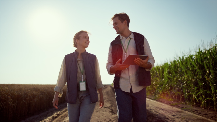 Smiling farmers walking farmland on sunny day. Happy agrarian team at field. Professional agritech engineer handsome man holding tablet computer. Two agronomists going ground road discussing work Royalty-Free Stock Footage #1089632587