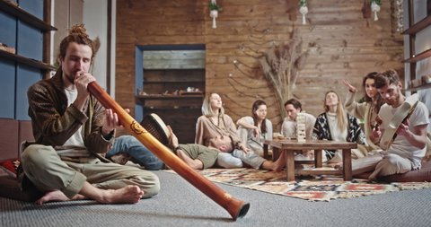 Hippies playing traditional musical instruments together. Group of friends playing authentic musical instruments and dancing while spitting on floor and chilling together in spacious room at home