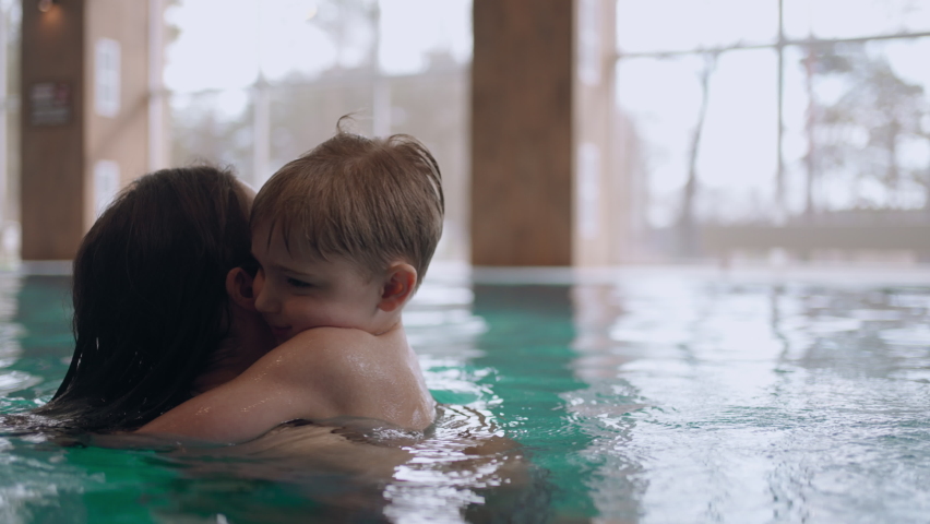 woman and her preschooler son are resting in water park, swimming in indoor pool
