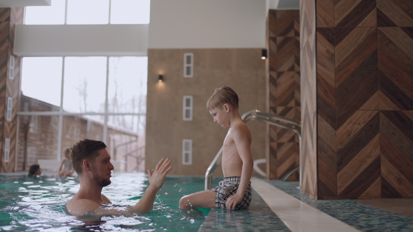 joyful little boy is playing with dad in swimming pool, rest in family wellness center in weekend