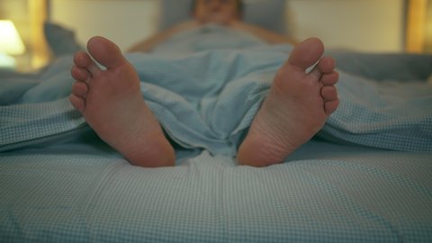 The feet of a man lying in bed at night under a blanket, close-up