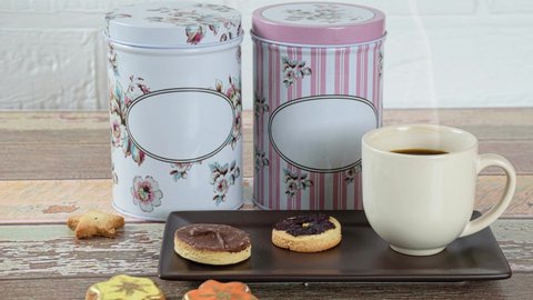Buttery biscuit with a dehydrated flower on top, next to other biscuits, cup of coffee and tins.