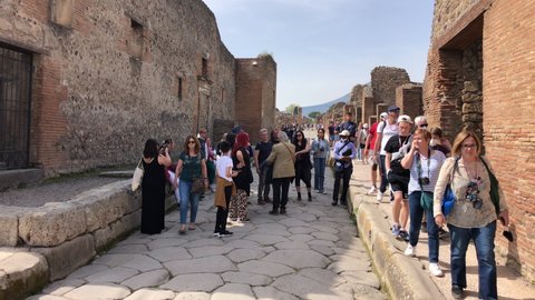 Pompeii, Naples - APR16, 2022: Pompeii guided tourists group tours in the ancient ruins sightseeing historic landmark of Pompeii, Italy. A lot of tourists explore the Ruins Of Pompeii.