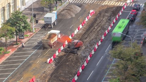 Industrial red excavator moving soil and loading into a dumper truck timelapse on road construction site. Aerial view of reconstruction of tram tracks