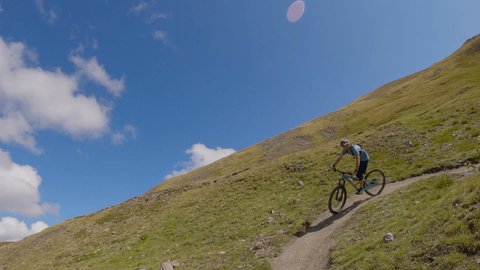 Man mountain biking surrounded by stunning mountain landscape. Tracking shot, man on a mountain bike descends technical terrain 