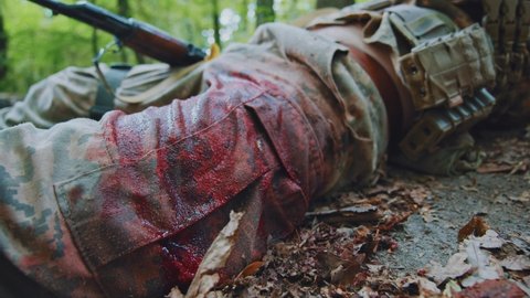 Close up leg soldier in camouflage uniform lying wounded blood around trying move near tree. In forest. War. Military concept