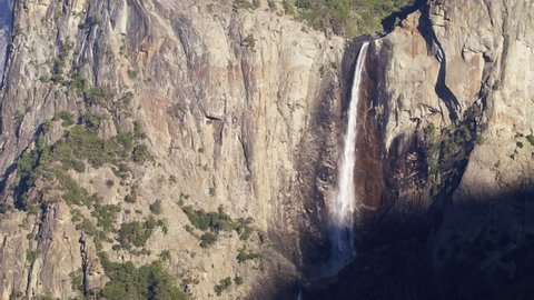Amazing Bridalveil Fall in Yosemite National Park, slow motion RED camera footage 6K. Beautiful waterfall in cinematic steep mountain cliffs with green pine forest on top of mountain, California USA