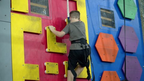 Child is training on the climbing wall. Children's rock climbing in a private school. Climbing exercises. School-age boy climbs the wall of a climbing wall.