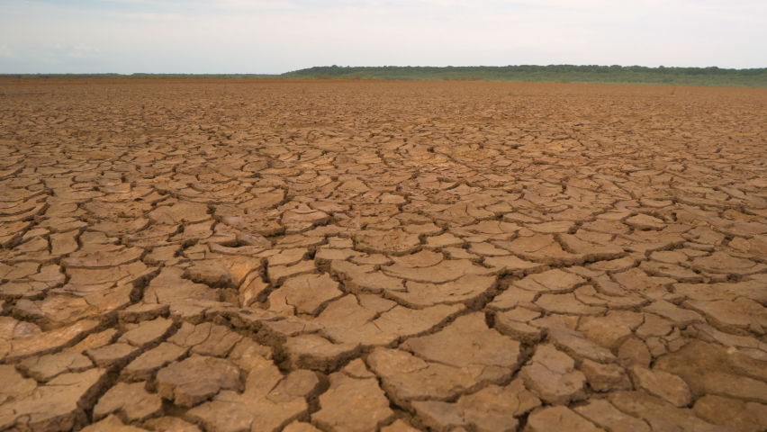 CLOSE UP: Big area of cracked soil caused by long draught. Brown desiccated land with ground cracks and no vegetation. Dry landscape with crack pattern caused by lack of water. Royalty-Free Stock Footage #1089642013