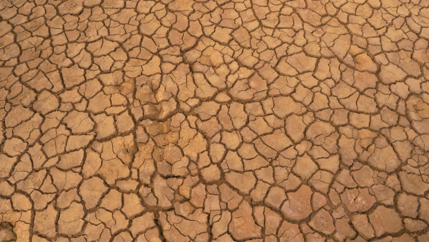 AERIAL TOP DOWN: Aerial top down view of cracked land caused by long draught. Brown desiccated soil with ground cracks and no vegetation. Dry landscape with crack pattern caused by lack of water. Royalty-Free Stock Footage #1089642017