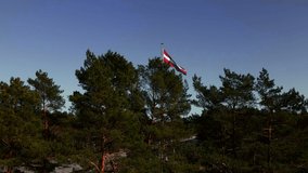 Establishing revealing shot of national Latvian flag behind trees with highway in background