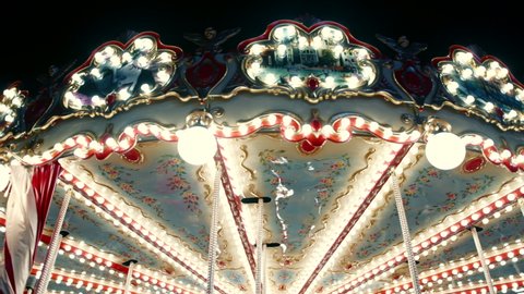 Medium shot of a beautiful old-fashioned spinning carousel attraction for kids with wooden horses and round light bulbs