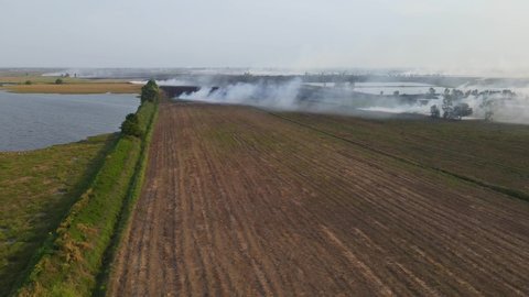 Descending aerial footage showing a tilled farmland and smoking rising making pollution in Pak Pli, Nakhon Nayok, Thailand.