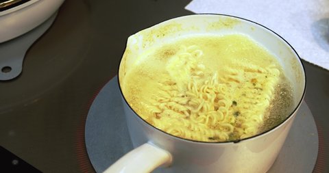 Man mixes instant Ramen to loosen the noodles in a boiled water in a white pan with chopsticks. A water is boiling by Induction heating (IH) system.