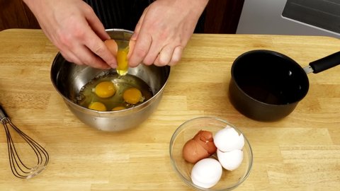 Home cooking - Cracking or adding whole eggs into stainless steel bowl in preparation of adding other ingredients to whisked to make omelet batter.