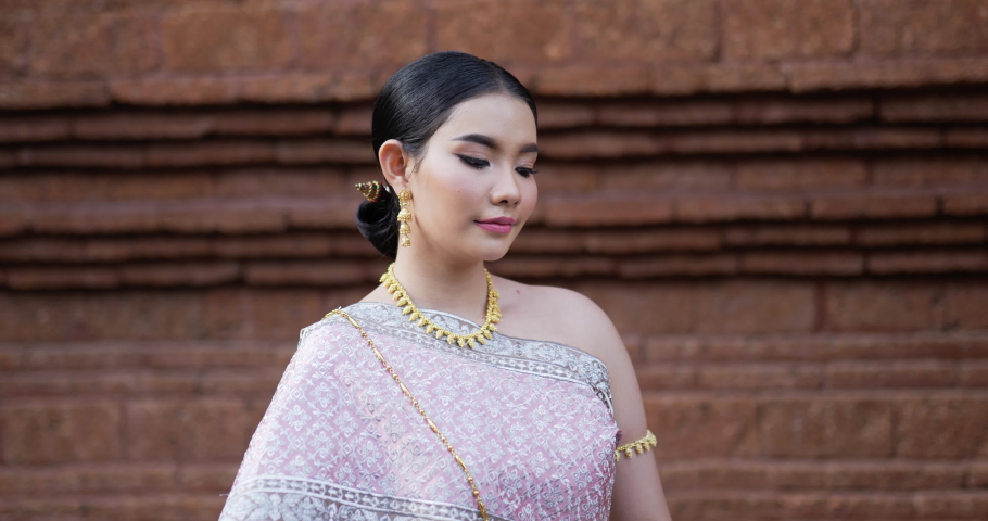 Portrait of Thai woman salute of respect in traditional costume of thailand. Young female looking at camera and smiling in ancient temple. Royalty-Free Stock Footage #1089649439