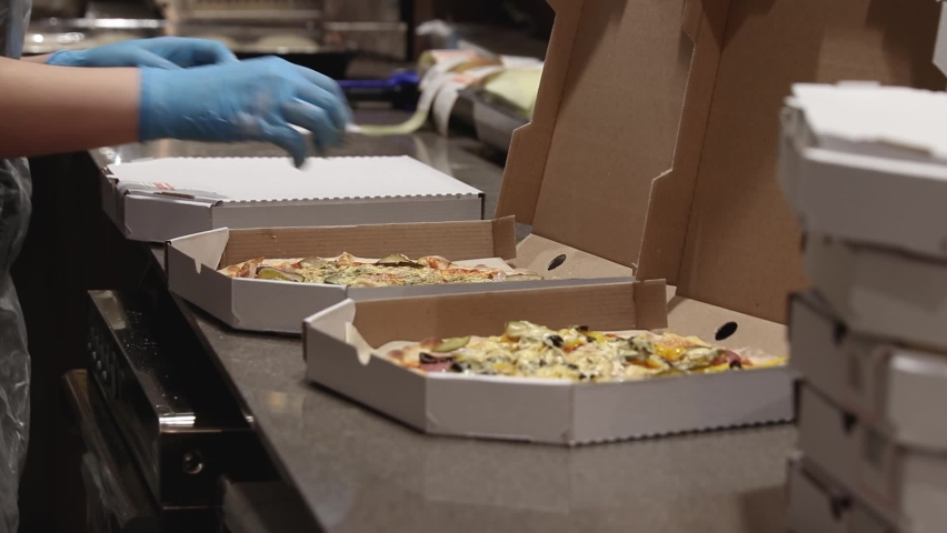 chef closes carton box with hot round pizzas and puts stickers on the package