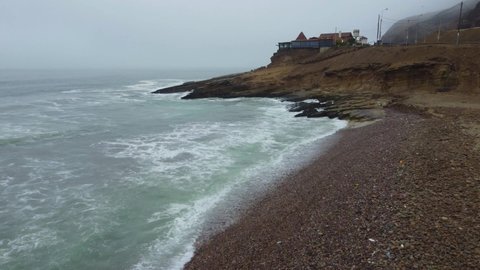 Drone video of a rocky beach shore flying towards a rocky outcrop on a foggy day.
