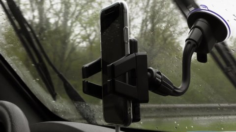 Closeup of a hand using a phone while driving in the rain.