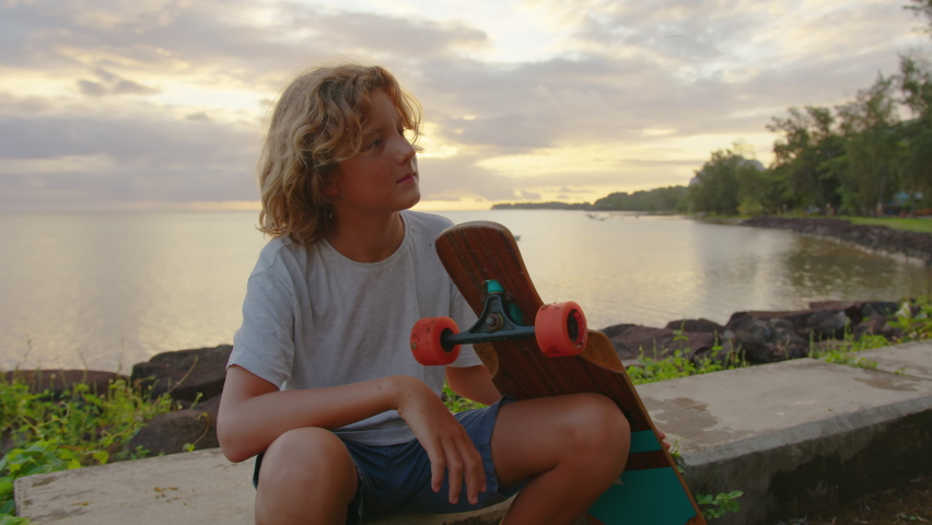 Silhouette, happy child portrait of young stylish skater boy holding his skateboard outdoors