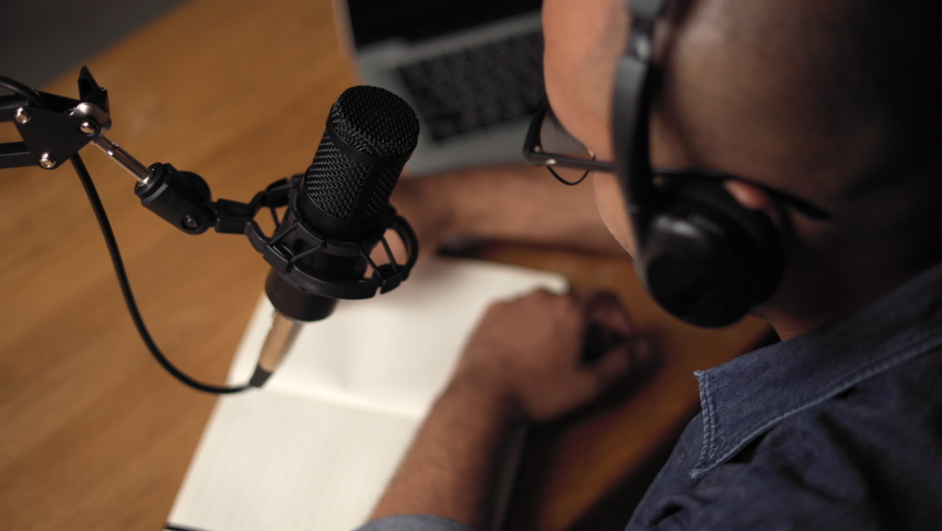 Close up hand take notes host streaming his a podcast on laptop with headphones and condenser microphone interview conversation at home broadcast studio. Male blogger recording voice over radio Royalty-Free Stock Footage #1089654823