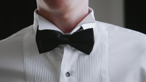 Successful elegant man going to a party and fixes bow tie around his neck by his hands. Element of men's wardrobe. Festive clothes for the official ceremony.