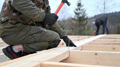 Man worker building wooden frame house on pile foundation. Carpenter hammering nail into wooden truss, using hammer. Carpentry concept.