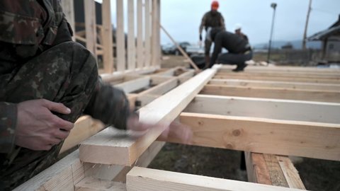 Men workers building wooden frame house on pile foundation. Carpenter installing wooden joist. Carpentry concept.