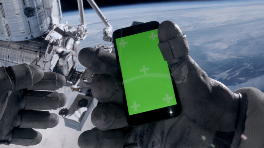 POV First person view through the astronaut helmet, astronaut using his mobile phone during the spacewalk. Green screen chroma key. ISS in the background. Some elements are furnished by NASA