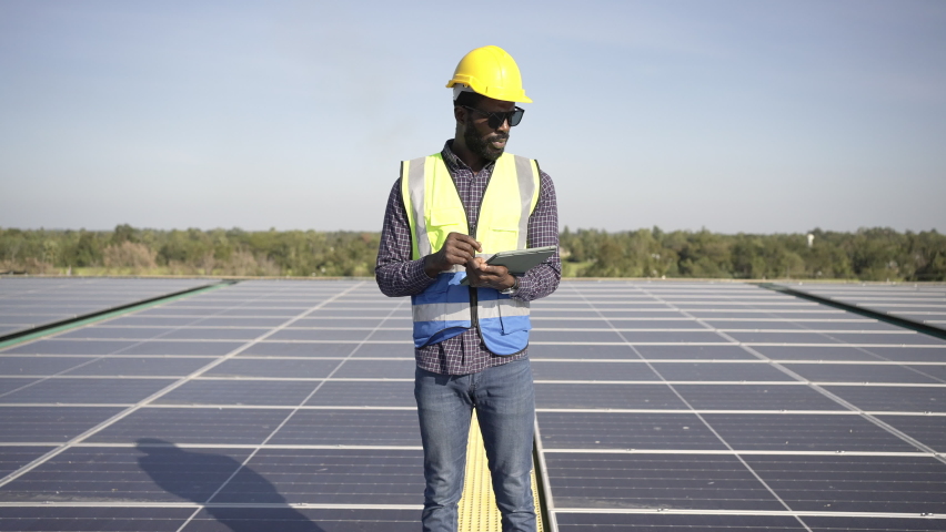 African man engineer using digital tablet maintaining solar cell panels on building rooftop. Technician working outdoor on ecological solar farm construction. Renewable clean energy technology concept Royalty-Free Stock Footage #1089659557