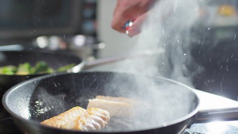Close up shot of chef using lighter to ignite fire in skillet and flambeing fish