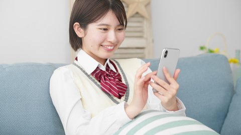 High school girl operating a smartphone on a sofa