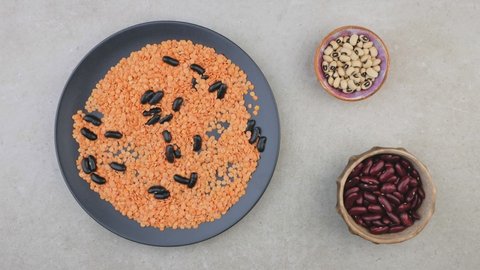 A wooden spoon composes the food sign with black beans in a bowl of orange lentils on a gray table. Symbol of a healthy lifestyle. Creates the atmosphere of a grocery store.