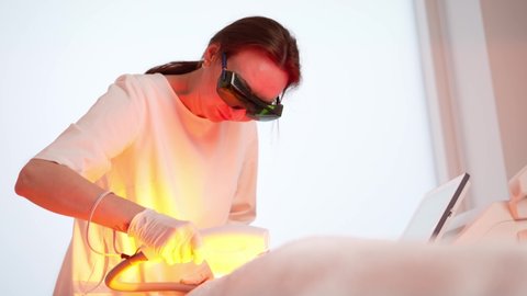 Not a young woman is receiving facial treatments in a beauty clinic. Woman beautician at work, laser skin treatment.